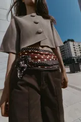 Chaqueta corta de punto color beige, con cuello redondo y manga tres cuartos. Cierre frontal con tres botones forrados a tono.