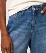 Bermuda de jeans azul oscuro, con trabillas en la cintura, bolsillos laterales y traseros, y cierre de botón y cremallera.