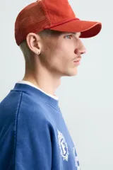 Sudadera de corte boxy fit en color azul con efecto lavado, cuello redondo y manga larga. Presenta estampado frontal con tipografía variada y gráficos estilo universitario. Interior afelpado y acabados en rib.