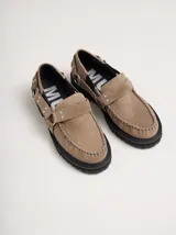 Mocasines de cuero color beige con plataforma negra, detalle de tira frontal con tachas metálicas y argollas laterales.