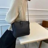 Cartera tipo bandolera de diseño estructurado, color negro, con cierre de solapa frontal mediante trabilla y correa ajustable para el hombro.