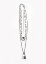 Collar de acero quirúrgico plateado con tres cadenas de diferentes largos y estilos. La cadena más corta tiene un dije de corazón negro, la más larga tiene un dije de candado plateado.