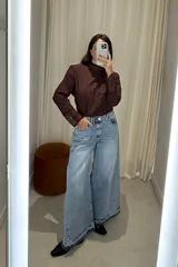 Blusa de manga larga color marrón oscuro, con cuello alto y diseño de encaje en los puños. Presenta un patrón de bordado inglés en toda la prenda, con mangas ligeramente abullonadas en los hombros.