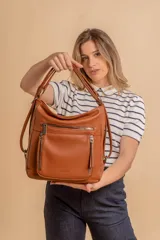 Cartera mochila de cuero sintético color suela, con diseño versátil que permite usarla como bolso de hombro o mochila. Presenta múltiples bolsillos frontales con cierre metálico y correas ajustables.