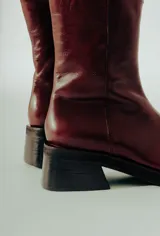 Bota de caña media confeccionada en cuero natural color bordó, con diseño minimalista, punta cuadrada y taco ancho de altura media.