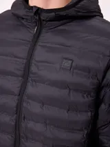Campera puffer negra con capucha, cierre frontal completo y bolsillos laterales con cierre. Diseño acolchado horizontal con logo de la marca en el pecho.