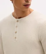 Remera de manga larga estilo Henley, confeccionada en tejido texturizado color beige, con cuello redondo y cierre frontal parcial de botones.