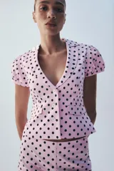 Chaqueta corta rosa con estampado de lunares negros, de cuello solapa y manga corta abullonada. Cuenta con falsos bolsillos con solapa en el delantero y cierre frontal con botones.