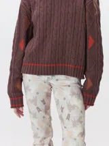 Sweater de punto con diseño de ochos en color verde, cuello redondo con detalle de franja en contraste, y apliques de rombos en las mangas. Presenta un bordado con la letra M en el pecho.