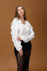 Blusa blanca de estilo romántico confeccionada en tela liviana, con mangas largas que presentan volados en toda su extensión y escote en V.