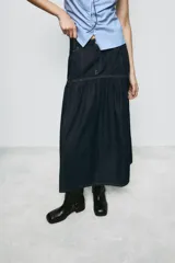 Falda midi de denim azul oscuro con tiro medio, bolsillos delanteros y costuras a contraste. Presenta un diseño con canesú estructurado y falda con frunces, cierre frontal con cremallera y botón metálico.