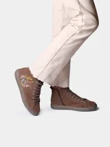 Botín de cuero serraje color beige, con cordones y detalle de flores bordadas en el lateral. Cuenta con suela plana de goma y cierre de cremallera lateral.