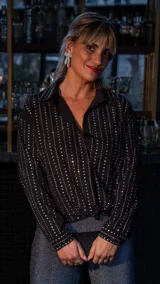 Camisa negra con cuello clásico, manga larga y cierre frontal con botones. Decorada con brillos plateados verticales.