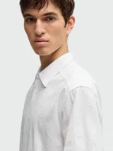 Camisa blanca de manga corta con cuello clásico y botones frontales. Presenta un tejido texturizado con finas rayas verticales en relieve.