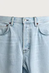 Jeans de corte barrel fit confeccionados en denim de algodón rígido, con diseño de cinco bolsillos y cierre frontal con botones. Presentan un lavado claro con efecto de roturas en las perneras.