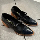 Zapato tipo Mary Jane de cuero vacuno con textura grabada, color marrón oscuro. Presenta una puntera cuadrada, taco bloque de madera y una tira con hebilla metálica sobre el empeine.