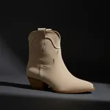 Botas texanas de caña corta, confeccionadas en material texturizado color beige, con diseño clásico de costuras decorativas, tiradores laterales y tacón cuadrado de madera.