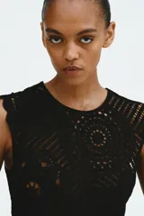 Top negro sin mangas de punto estilo crochet, con cuello redondo, cierre oculto en la espalda y diseño de peplum acampanado con ribetes festoneados.