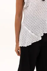 Blusa de textura rugosa en color blanco, sin mangas, con detalle de volados en los hombros y corte asimétrico en el ruedo.