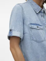 Vestido corto de denim en tono celeste claro, con cuello camisero, cierre frontal con botones metálicos, bolsillos con solapa en el pecho y mangas cortas con vuelta.