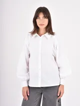 Camisa blanca de corte clásico con cuello camisero y cierre frontal de botones. Presenta mangas largas abullonadas con puños ajustados y detalle de frunces en los hombros.