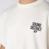 Remera oversize color blanco de interlock con sisas al corte, cuello redondo y estampa pequeña frontal con texto en negro.