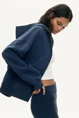 Campera canguro de felpa color azul marino con cierre frontal, capucha forrada y bolsillos delanteros tipo parche. Presenta hombros caídos, corte holgado y puños y bajo de punto acanalado.