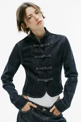 Cazadora de denim azul oscuro, de corte entallado, cuello redondo y manga larga. Cuenta con cierre frontal con alamares y costuras pespunteadas en contraste.