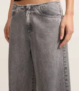 Pantalón de jean gris de tiro bajo y corte amplio, sin pretina, con cierre tradicional y bolsillos.