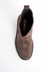 Bota tipo Chelsea de caña media, confeccionada en gamuza color marrón. Presenta paneles laterales elásticos al tono y una suela de goma robusta con plataforma baja y taco cuadrado.