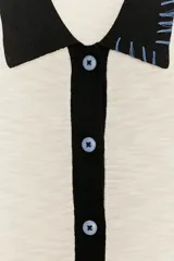 Chaqueta de punto de manga larga con cuello solapa y cierre frontal de botones. Presenta un diseño de bloques de color: cuerpo principal color crema, manga izquierda negra, manga derecha azul claro y cuello negro. Incluye detalles de costura expuesta en azul claro en el cuello y el bajo.