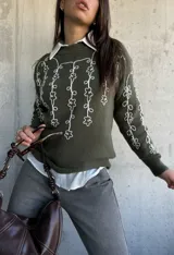 Sweater de punto color verde oliva con cuello redondo y diseño de flores bordadas en hilo blanco en el frente y las mangas.