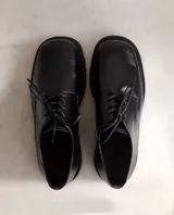 Zapato acordonado de cuero negro con punta cuadrada y suela track.