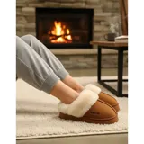 Pantuflas de gamuza negra con plataforma, forradas internamente con corderito sintético color crema. Presentan un diseño sin talón y detalle bordado en el empeine.