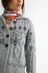 Saco de punto con cuello tipo polo, cierre frontal de botones oscuros y diseño de estampado jacquard en tonos grises y beige. Presenta mangas largas con puños acanalados y textura suave.
