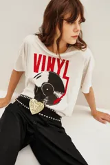 Remera de algodón blanca, corte holgado, con cuello redondo. Presenta un estampado frontal grande con la palabra "VINYL" en rojo y la ilustración de un disco de vinilo en negro y rojo.