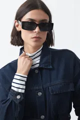 Sobrecamisa de jean color negro con silueta relajada, cuello camisero, cierre frontal con botones metálicos, bolsillos frontales y cinturón ajustable en la cintura.