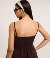 Top marrón oscuro con escote recto y breteles finos. Presenta un efecto drapeado en el torso y un peplum con volados en el bajo.