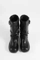 Bota media de cuero vegano color negro, con taco cuadrado y puntera redondeada. Cuenta con detalles de hebillas metálicas y correas decorativas en la caña y alrededor del tobillo.
