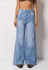 Pantalón de jean estilo wide leg color celeste claro, con tiro alto y cierre frontal con botón. Presenta una abertura lateral en cada pierna decorada con botones metálicos a lo largo de toda la extensión.