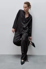 Pantalón de pierna amplia y calce holgado, color negro, confeccionado en tejido satinado. Cuenta con cintura elastizada, recortes horizontales y tiras regulables en los ruedos.