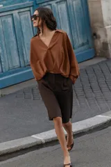Camisa de lino color beige, con cuello solapa, escote en V y mangas largas. Presenta un diseño de bajo asimétrico con pliegues delanteros que generan un efecto abullonado.