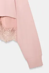 Sudadera crop de cuello redondo y manga larga con puños elásticos. Presenta un diseño de doble capa con un top interior satinado y un bajo decorado con encaje a tono.