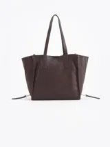 Bolso tipo tote de cuero color tostado con doble asa de hombro, detalles de hebillas metálicas en el frente y cierres laterales decorativos.