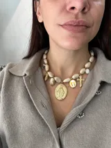Collar corto compuesto por cuentas de resina en tono crema con acabado marmolado, adornado con múltiples dijes colgantes de acero dorado que incluyen una medalla de la Virgen Milagrosa, una cruz y un dije circular con flores pintadas.