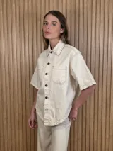 Sobrecamisa de manga corta color beige, confeccionada en denim soft, con bolsillos frontales con solapa, cuello camisero, botones oscuros y pespuntes en contraste.
