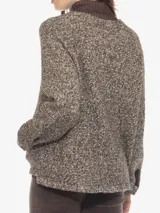 Sweater de tejido grueso jaspeado en tonos marrones y beige, con cuello alto de pana marrón oscuro y cierre frontal parcial con botones a presión. Posee un bolsillo canguro en la parte delantera.