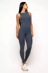 Jumpsuit deportivo de una pieza, color gris oscuro, con cuello alto, sin mangas y diseño ajustado. Presenta un escote profundo en la espalda y costuras estratégicas que realzan la silueta.