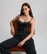 Corset negro con busto de media copa, confeccionado en poliamida con detalles de encaje en el escote y recortes laterales de tul transparente. Cuenta con tirantes finos ajustables y varillas internas para estructura.