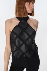 Top de cuello halter confeccionado con parches de cuero negro unidos mediante tejido de punto a crochet, creando un diseño geométrico de rombos.
